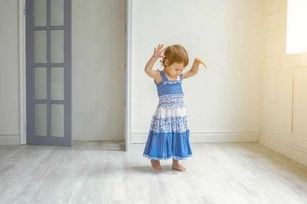 little cute sweet smiling girl in blue dress dancing in bright light living room at home and laughing. childhood, preschool, youth, relax concept