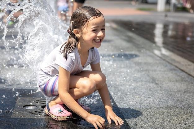 happy little girl among the splashes of water of the city fountain.